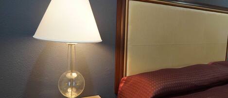 Ein Hotelzimmer mit Nachttischlampe, einem Bett mit Kopfteil und einem Nachttisch.