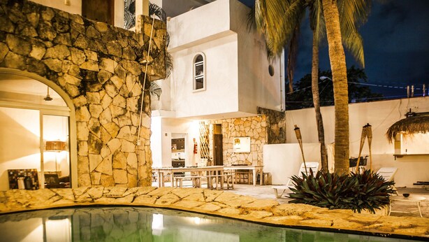A pool area with stone walls, a bar, and lounge chairs. - Hostal Inn - Hostel (Playa del Carmen)