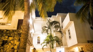 A multi-story building with a stone facade, palm trees, and a night sky. - Hostal Inn - Hostel (Playa del Carmen)