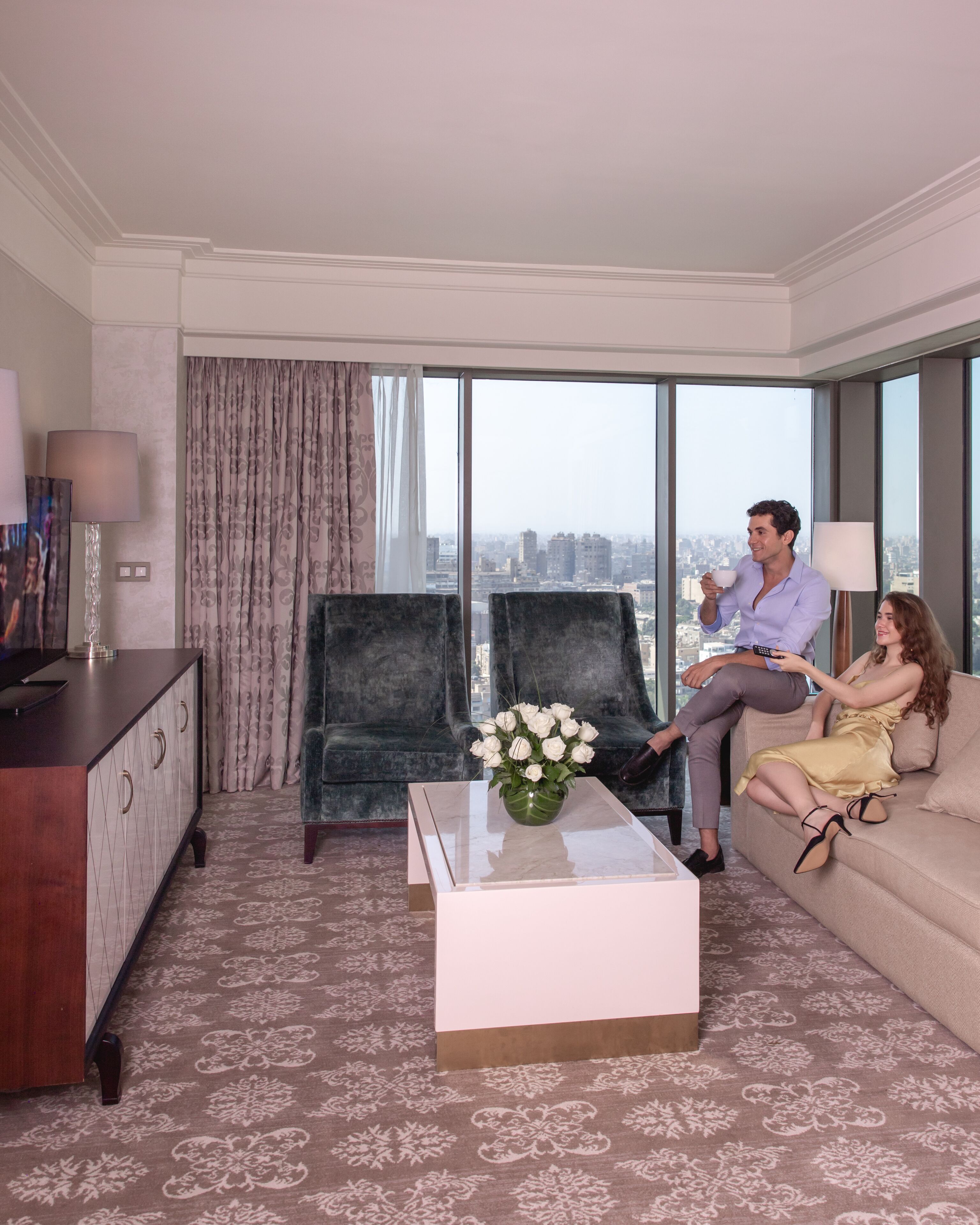Een moderne hotelkamer met een groot raam, een bank, een bijzettafeltje met een bloevas, en een kast.