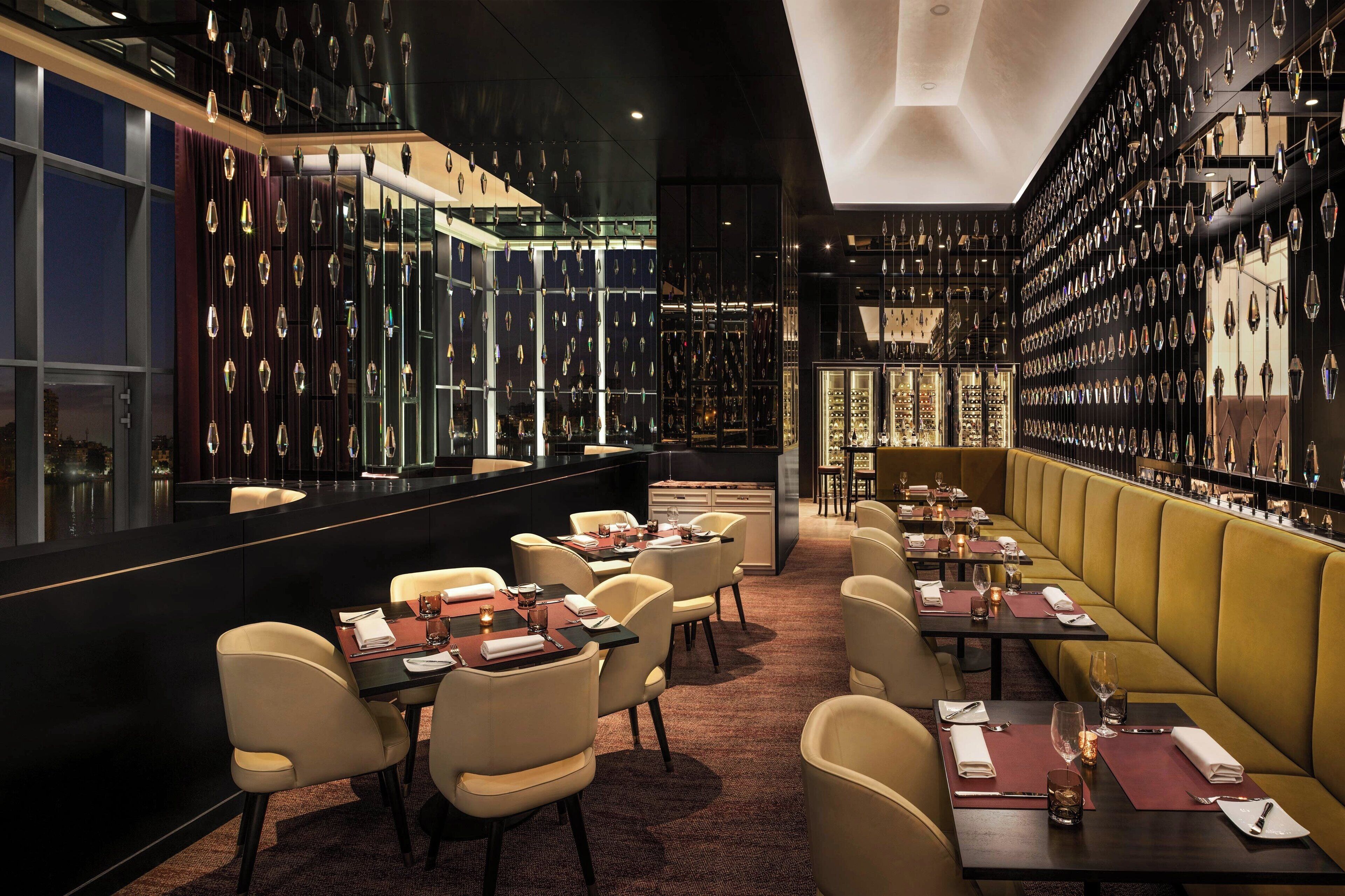Un restaurant au décor moderne, avec un bar agrémenté de décorations en cristal suspendu et un espace salon doté de banquettes moelleuses et de tables.