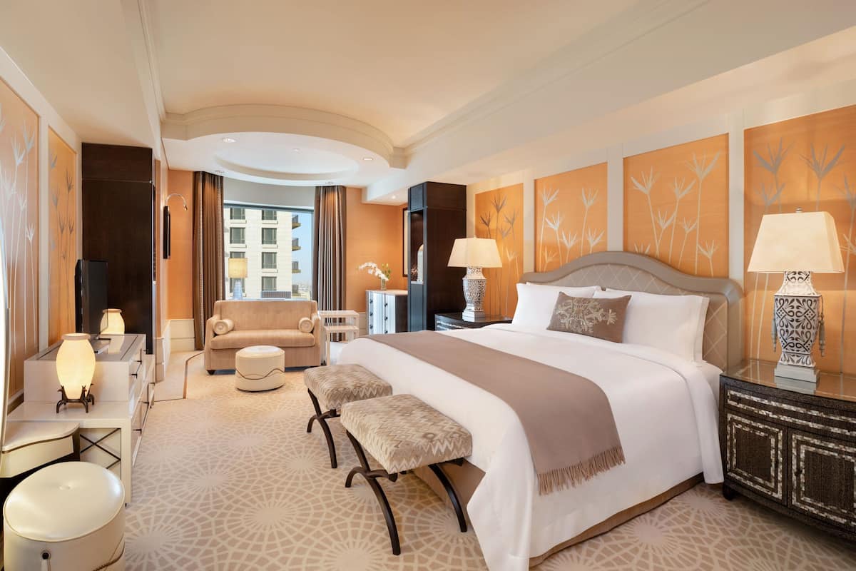 Habitación de hotel con una cama grande, un sofá, un escritorio con lámpara y vistas a la ciudad por la ventana.