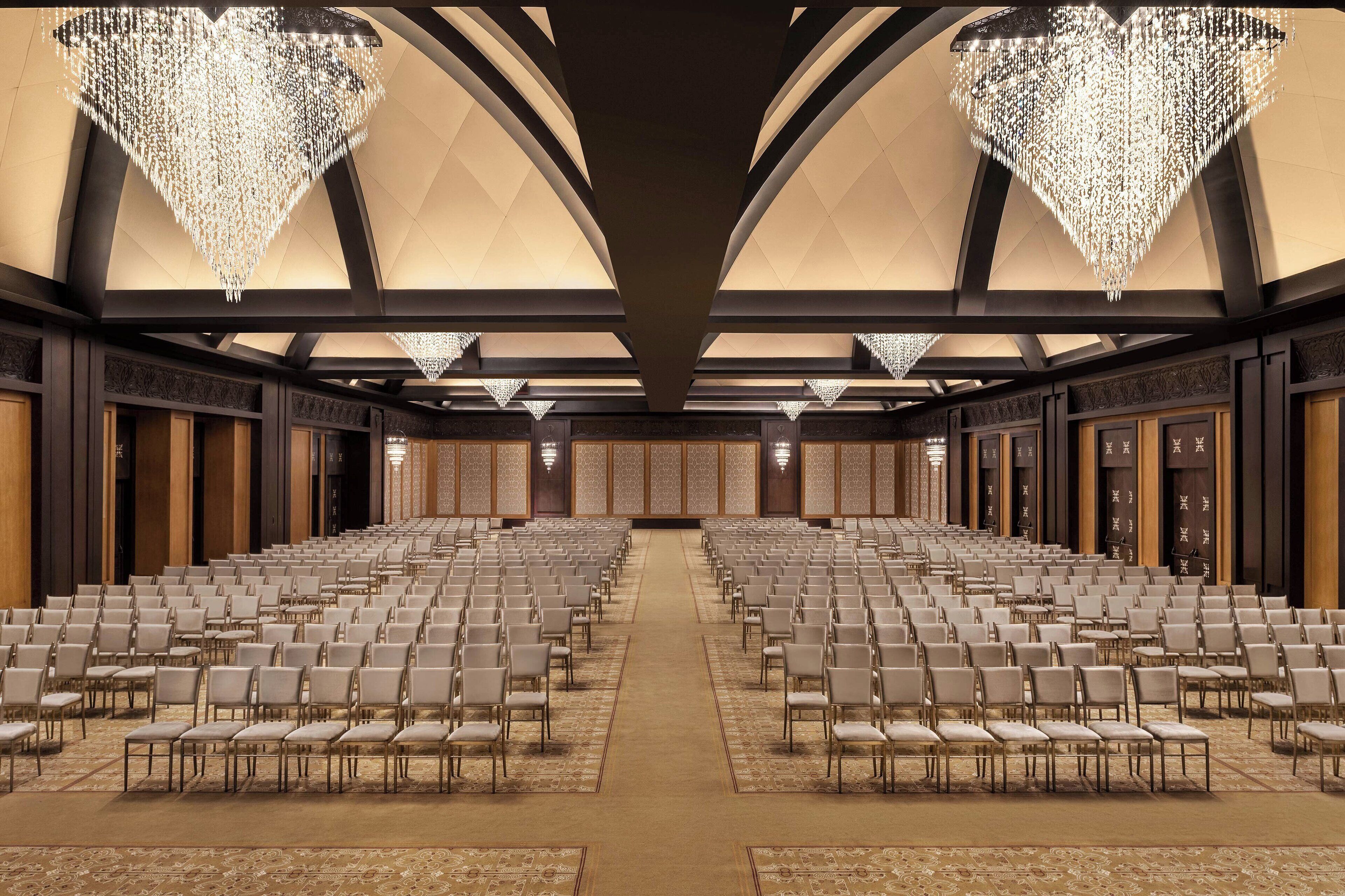 Un amplio salón de conferencias con filas de sillas, un techo alto con candelabros y piso alfombrado.