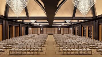 Un amplio salón de conferencias con filas de sillas, un techo alto con candelabros y piso alfombrado.