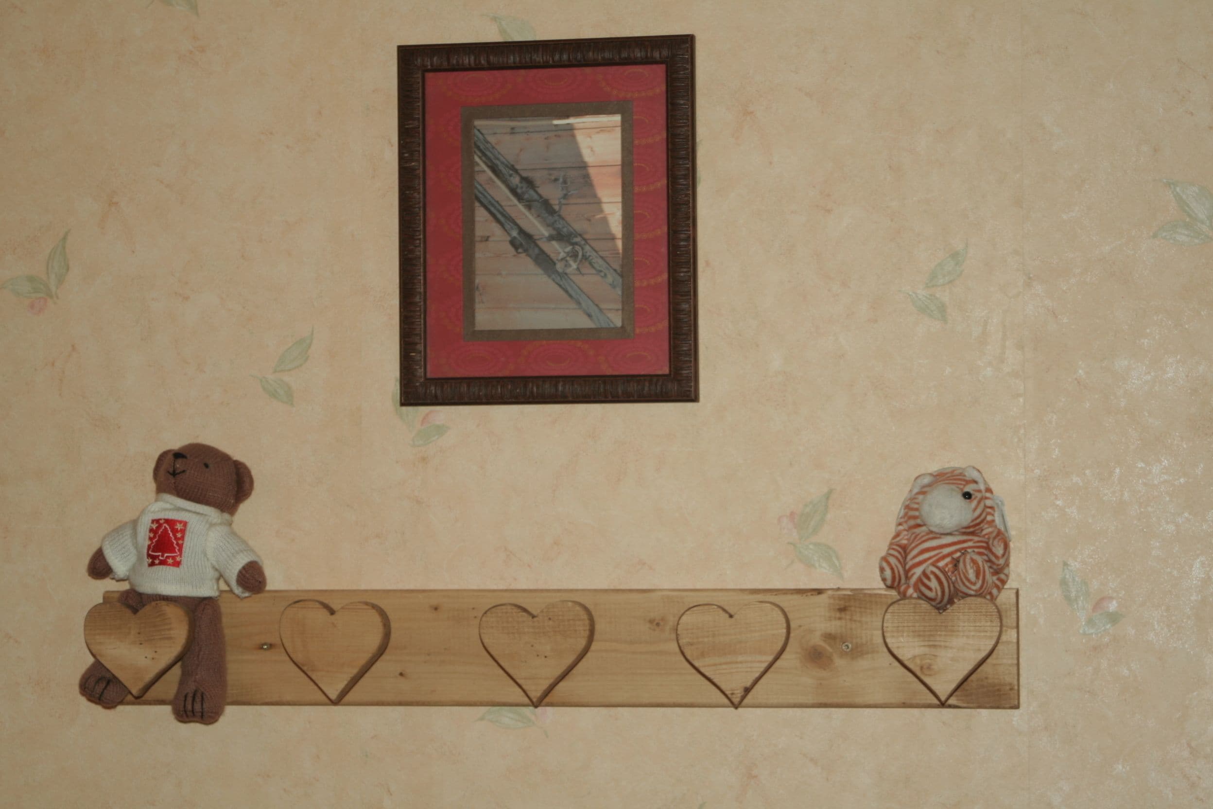 A wall with a framed picture, a shelf with heart-shaped decorations, and a teddy bear and a bird figurine.