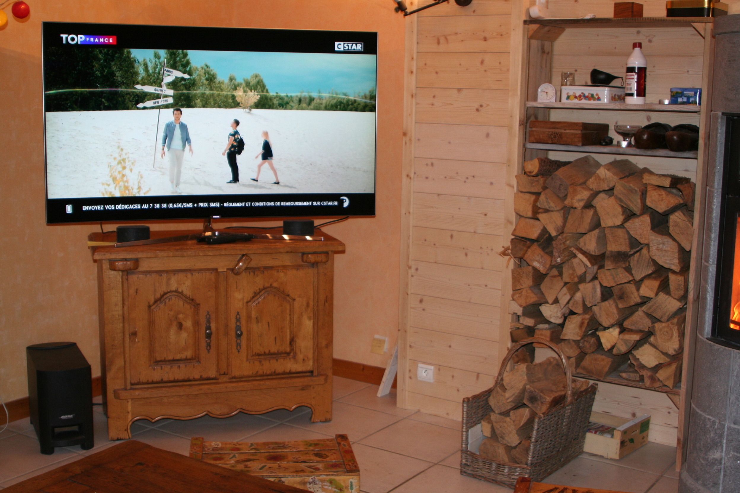 A television displaying a program, a wooden cabinet, a fireplace with logs, and a wicker basket.