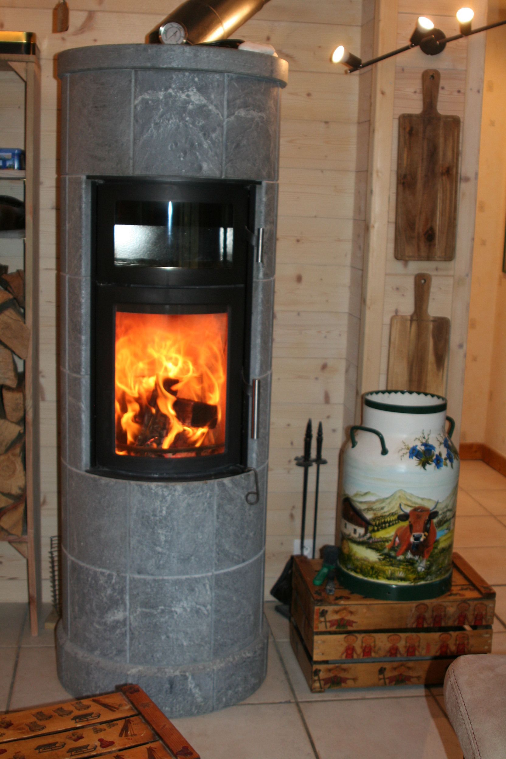 Una chimenea de piedra con fuego encendido, una tabla de cortar de madera rústica y un jarrón decorativo con una ilustración de vaca.