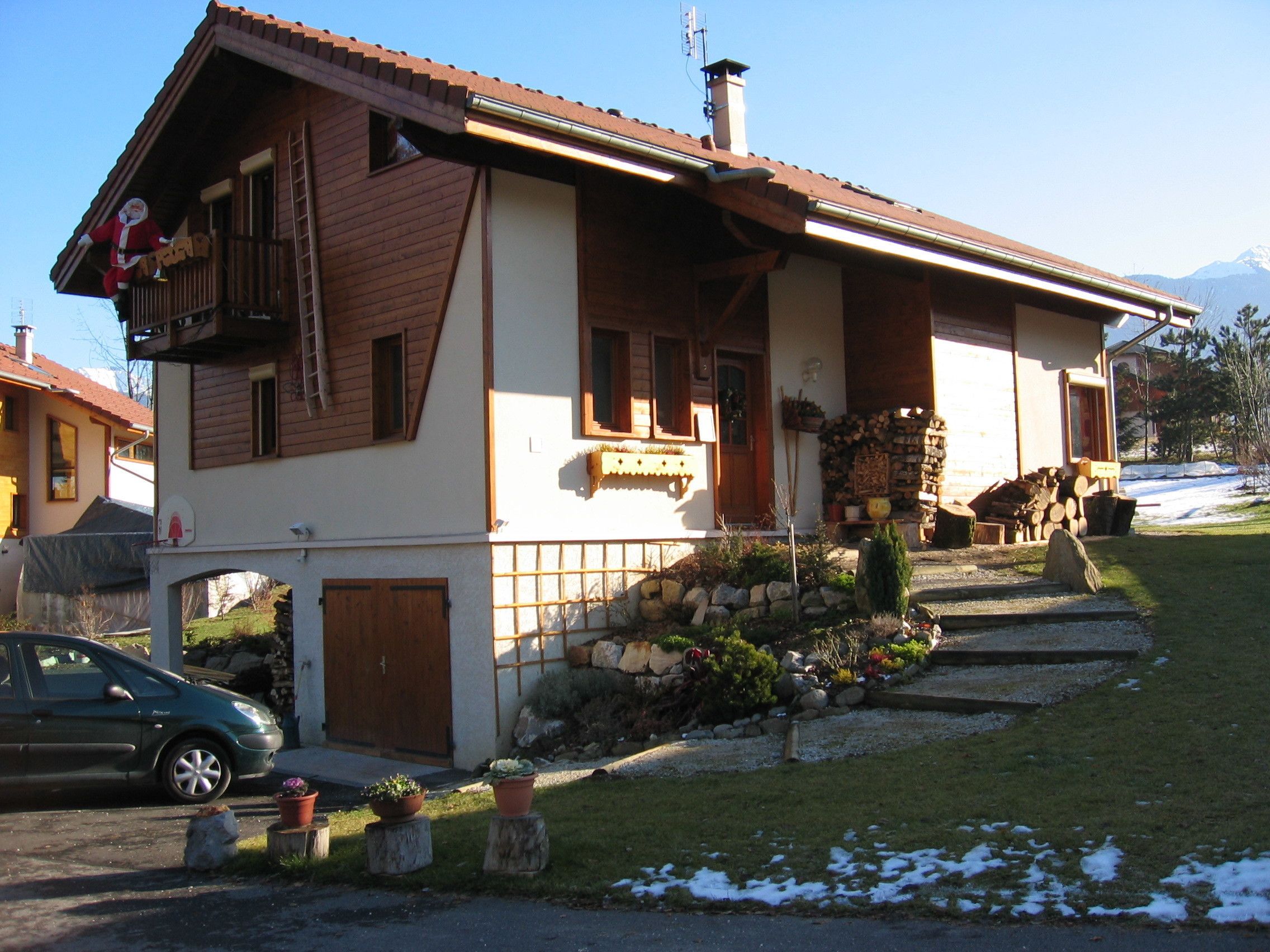 Ein zweigeschossiges Haus mit Holzfassade, einem Balkon im oberen Stockwerk und einer Steinmauer davor.