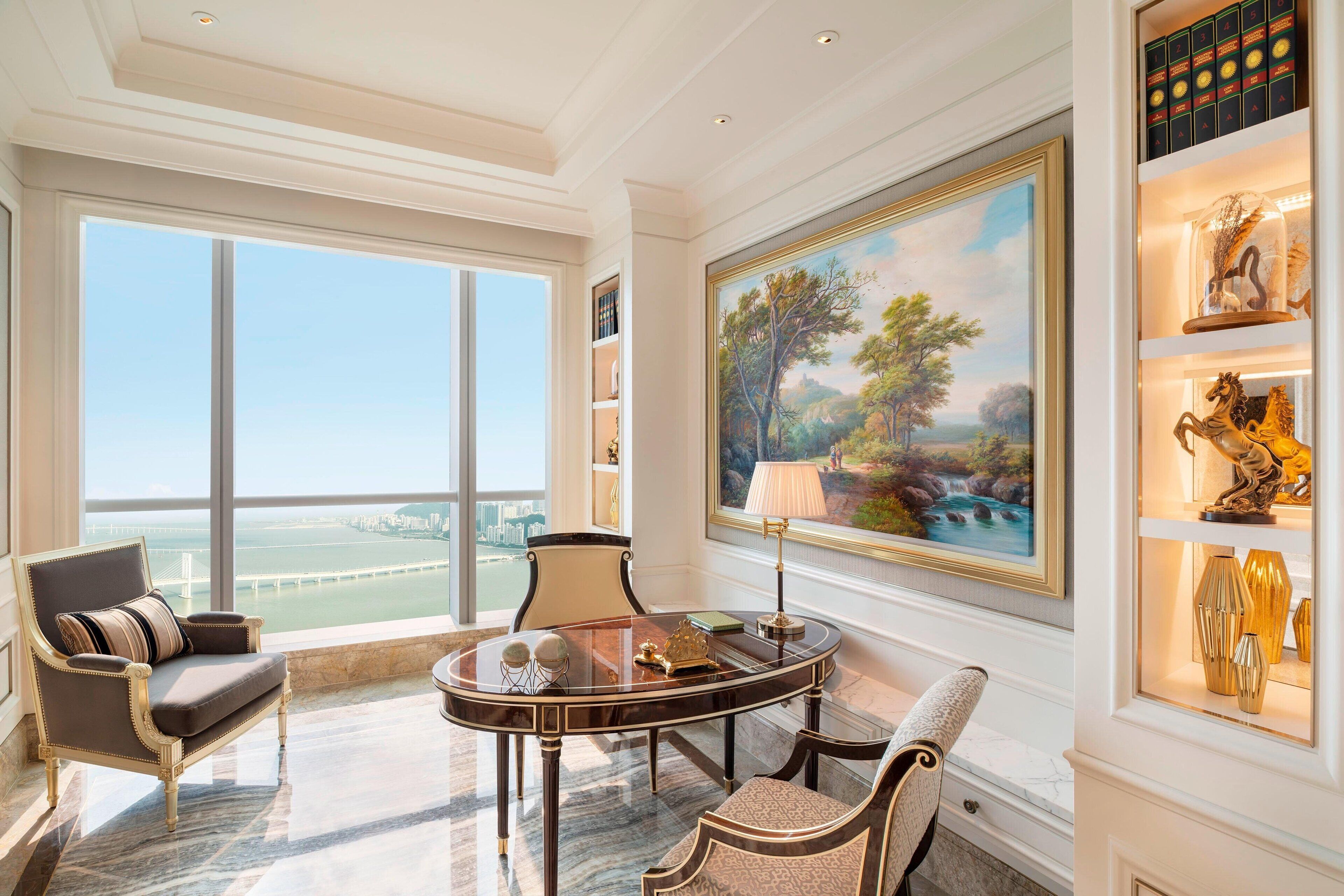 Um quarto luxuoso com uma grande janela que oferece vista para a cidade, piso de mármore, uma mesa redonda com luminária e uma estante com objetos decorativos.