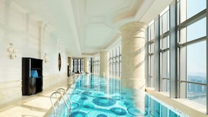 A spacious indoor swimming pool with a patterned floor, large windows, and a view of the city.