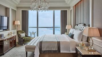 Amplia habitación de hotel con una cama grande, televisión, candelabro y vistas de la ciudad a través de amplias ventanas.