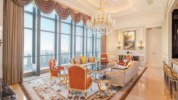 A luxurious living room with a large glass coffee table, elegant chairs, and a chandelier.