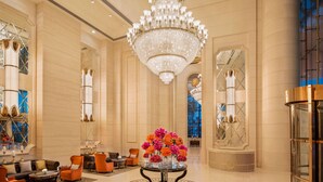 A spacious lobby with a large chandelier, elegant seating, and a central table with flowers.
