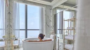 A spacious bathroom with a large bathtub, marble flooring, and a view of the city through large windows.