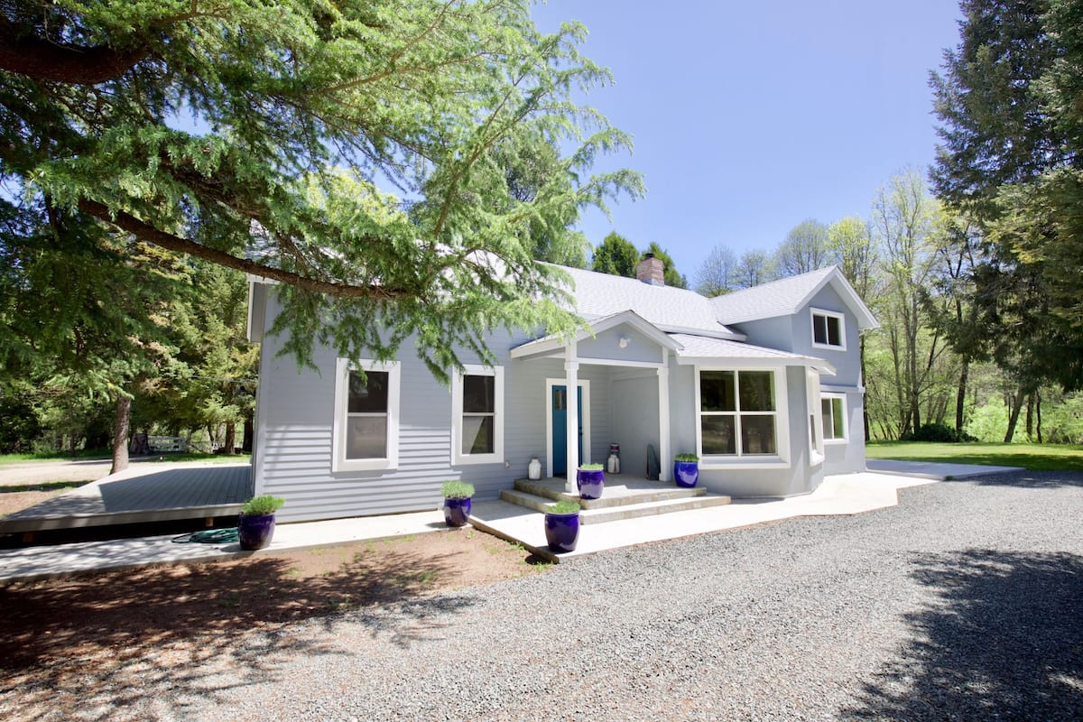 A modern two-story house with a covered porch, a gravel driveway, and potted plants.