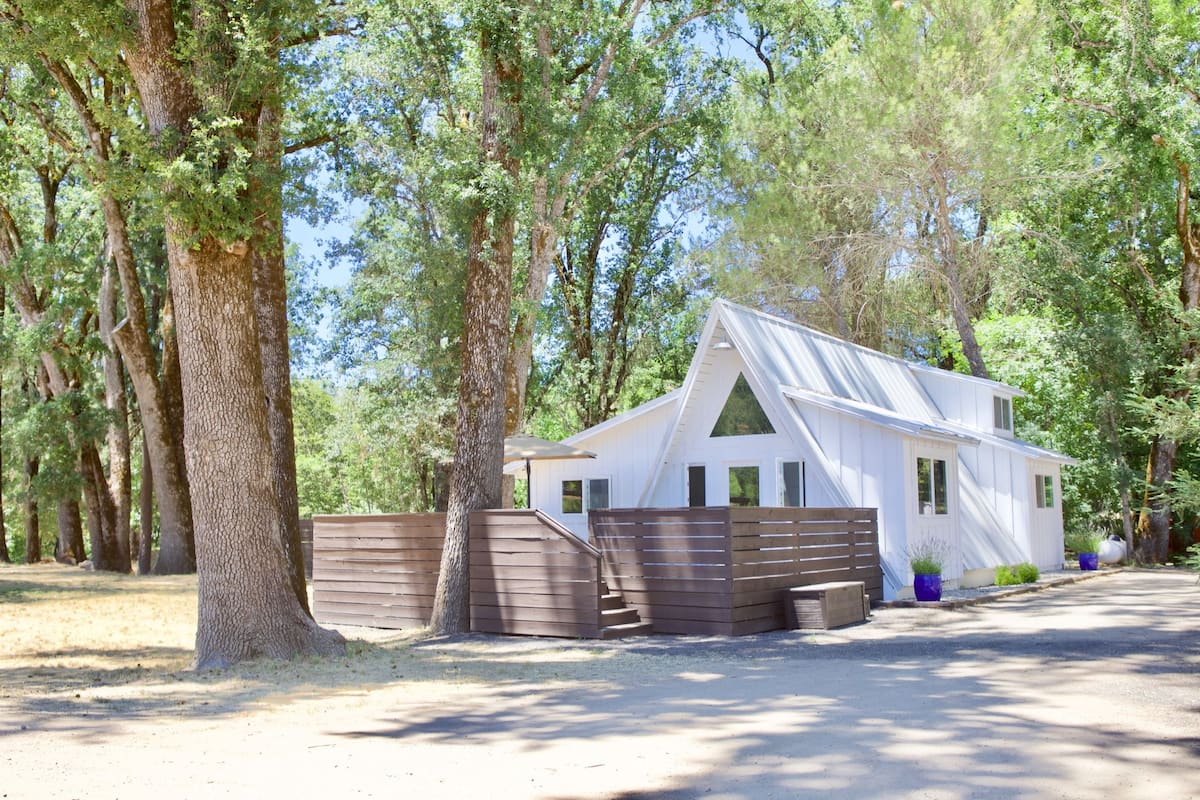A white cabin with a sloped roof, surrounded by trees.