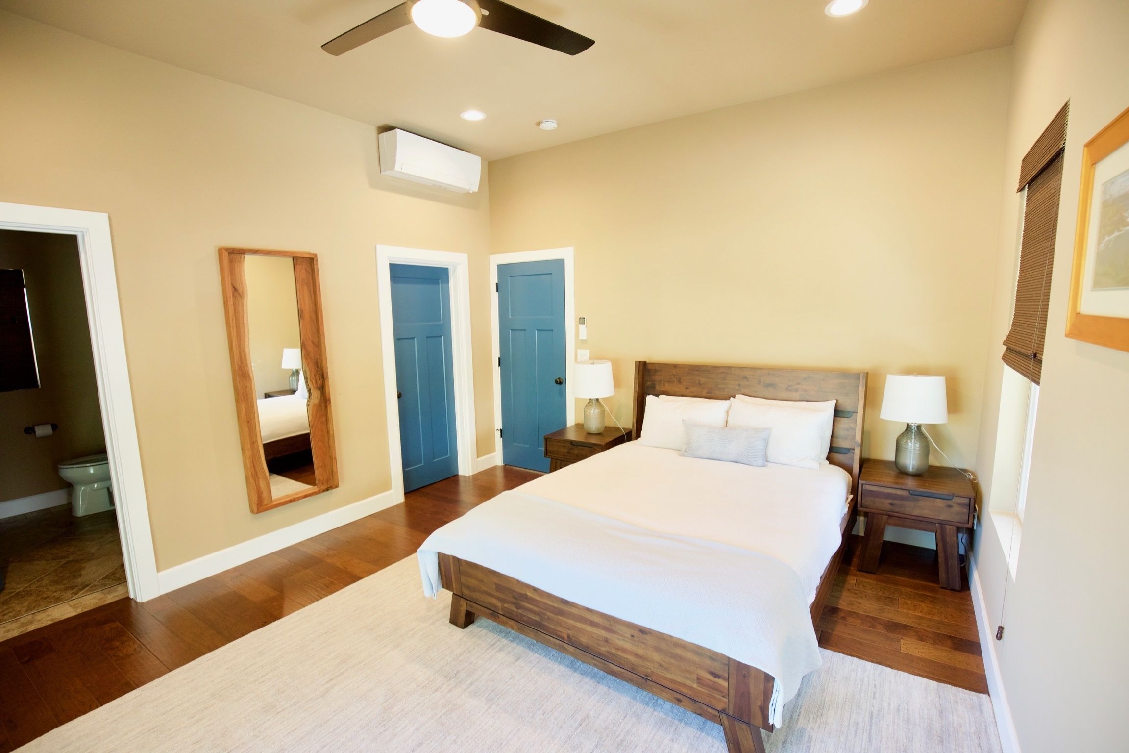 A bedroom with a large bed, wooden headboard, two bedside tables with lamps, a ceiling fan, and a mirror on the wall.