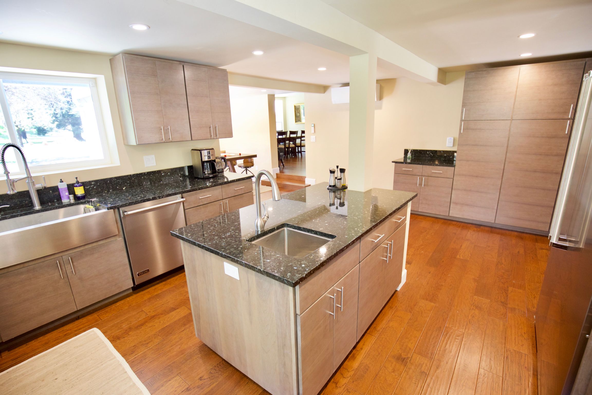 A modern kitchen with wooden cabinets, a granite countertop, stainless steel appliances, and a wooden floor.
