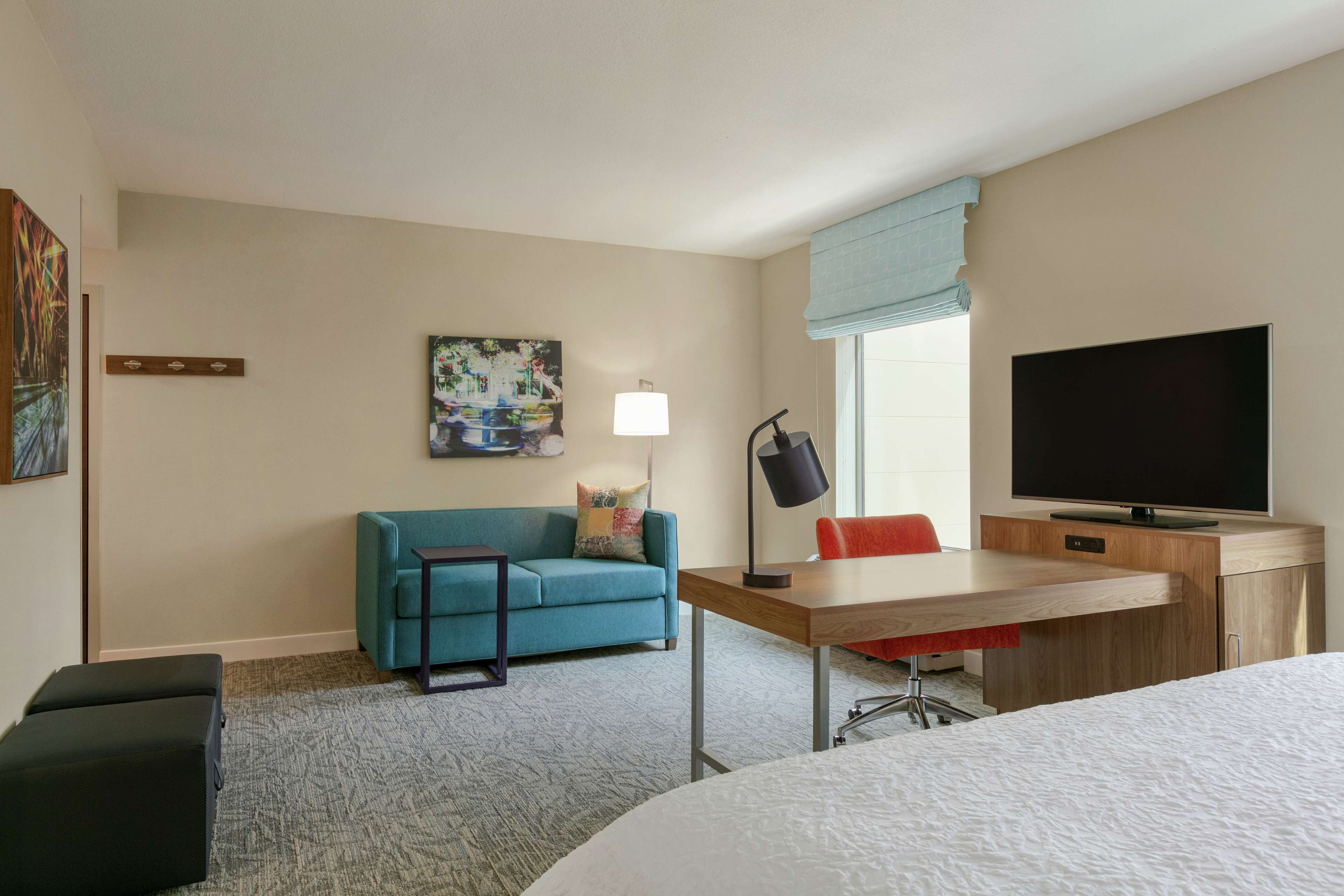 Habitació d'hotel amb llit, escriptori amb cadira, sofà, televisió i làmpada.