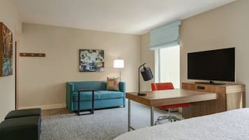 Habitació d'hotel amb llit, escriptori amb cadira, sofà, televisió i làmpada.