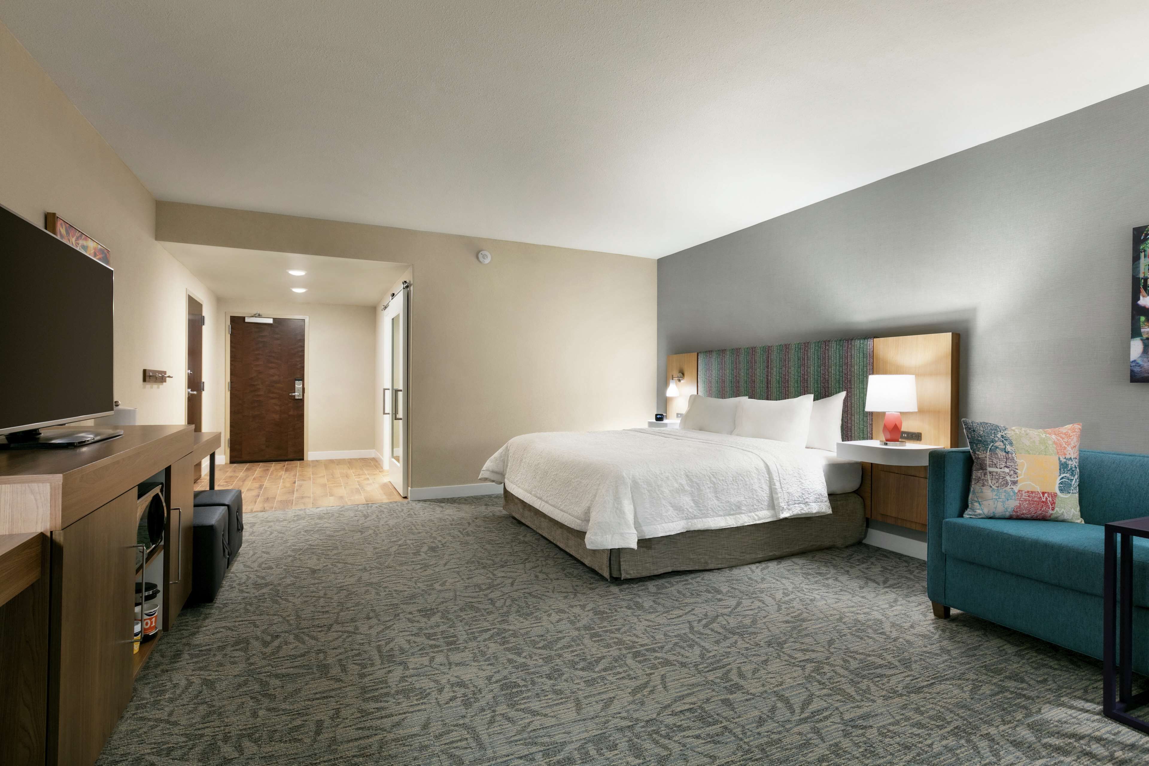 A hotel room with a bed, a TV, a desk with a computer, a sofa, and a lamp.