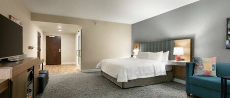 A hotel room with a bed, a TV, a desk with a computer, a sofa, and a lamp.