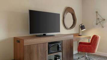 Una habitación de hotel moderna con un escritorio de madera, un televisor de pantalla plana, un microondas, una cafetera y una silla de oficina roja.