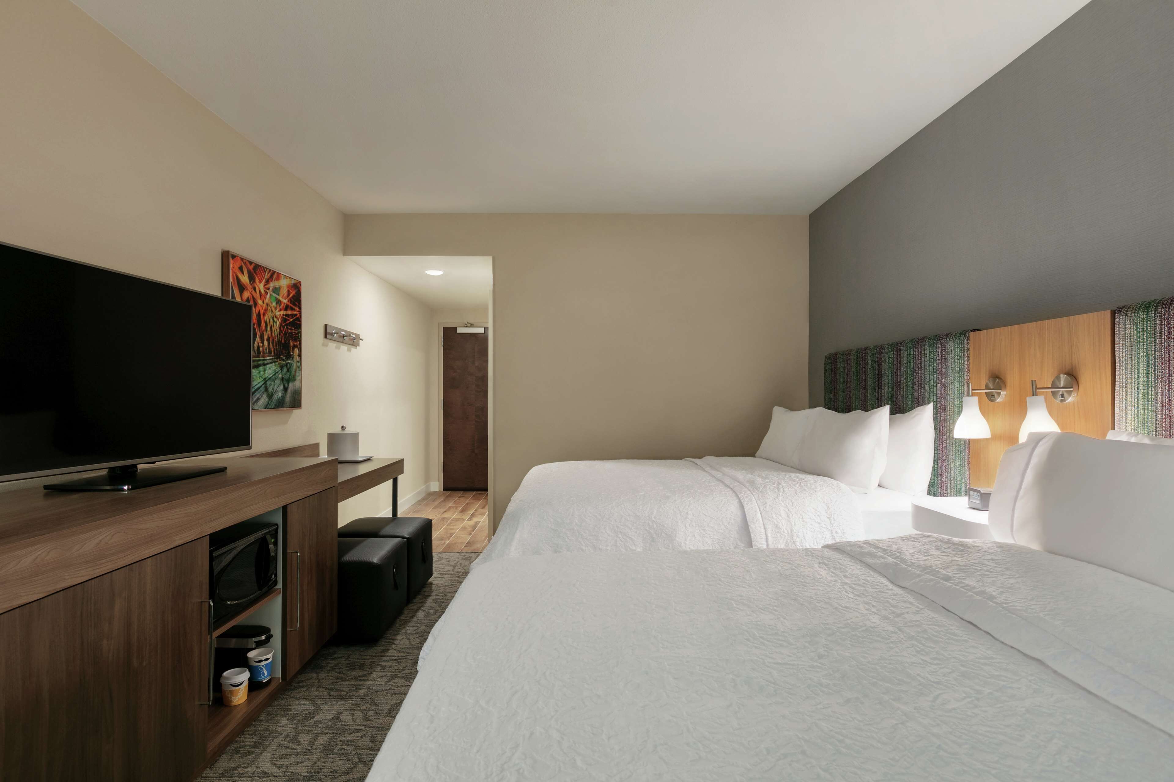 Habitación de hotel con televisión de pantalla plana, una cama, escritorio con microondas y una pequeña kitchenette.