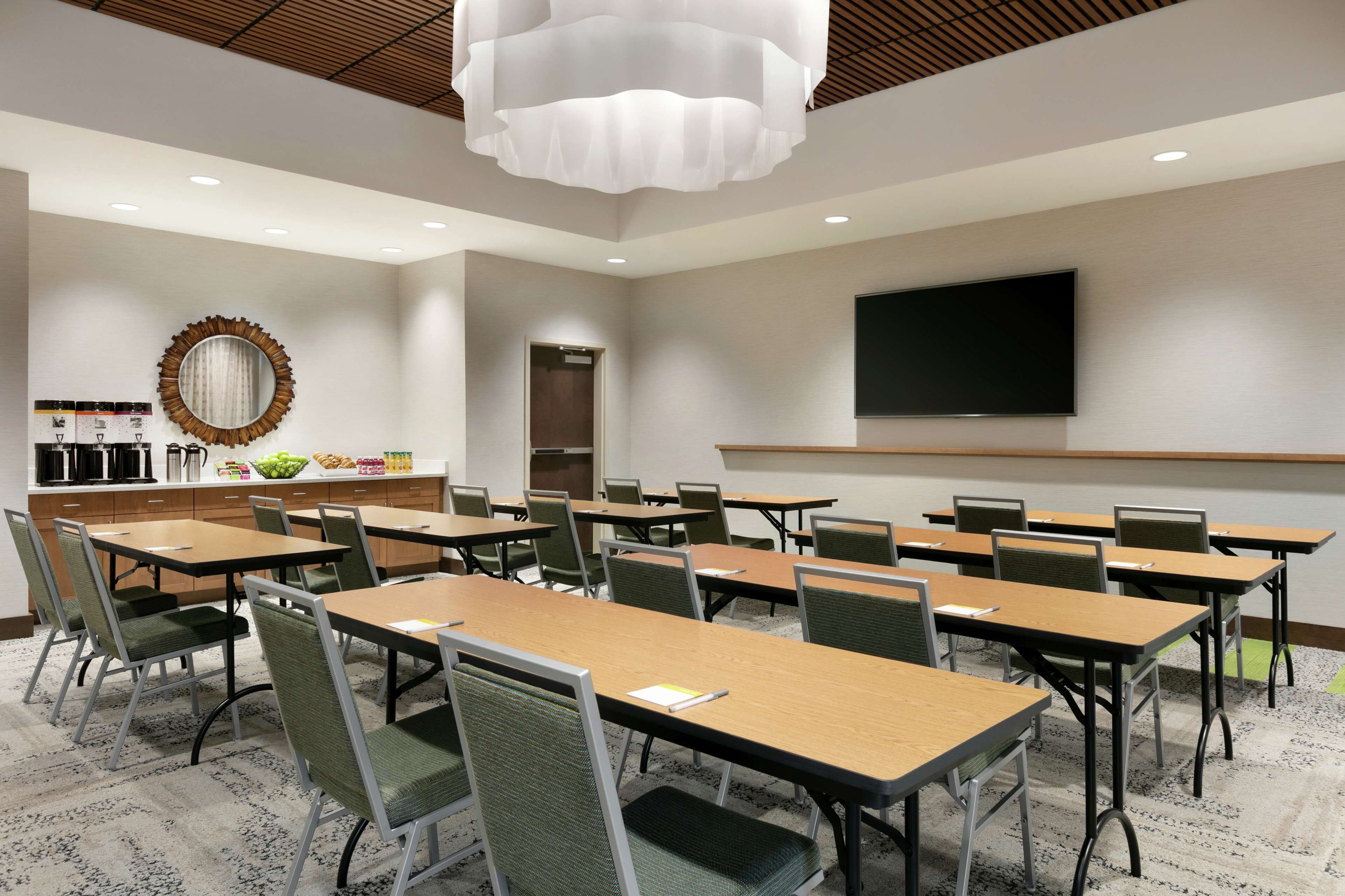 A conference room with tables and chairs, a large mirror, a television, and a kitchenette area.