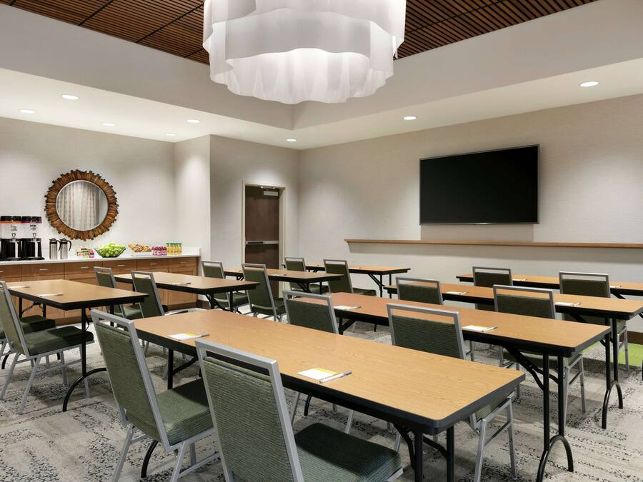 A conference room with tables and chairs, a large mirror, a television, and a kitchenette area.