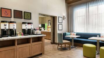 A modern hotel room with a kitchenette, a seating area with a sofa and ottomans, and artwork on the walls.