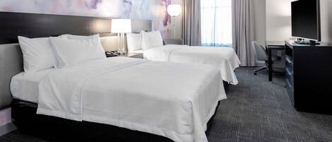 A hotel room with two beds, a desk, a television, and a large window with curtains.