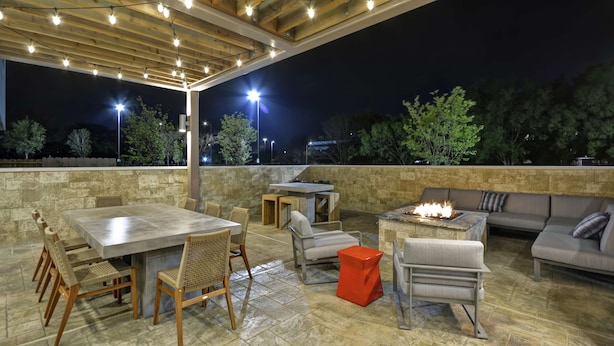 Un espace extérieur aménagé en terrasse, avec un mur en pierre, une pergola en bois et des guirlandes lumineuses.
