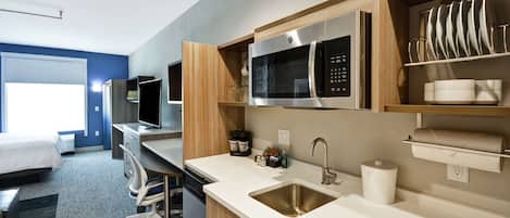 A modern hotel room with a kitchenette, a bed, a desk, and a television.