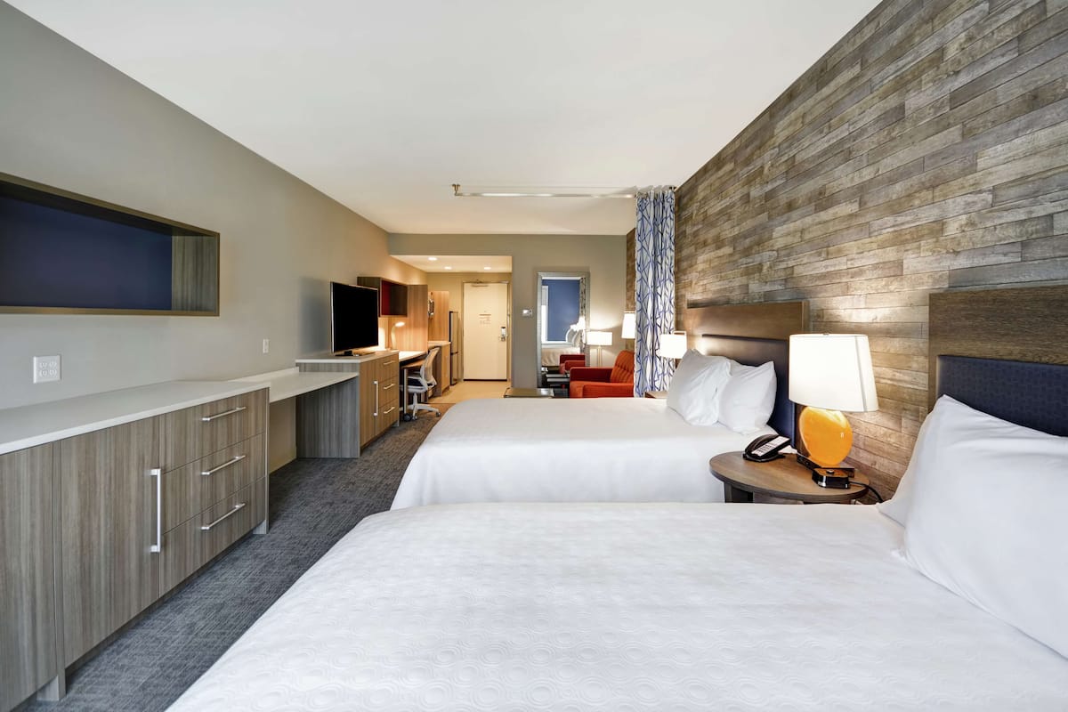 A hotel room with two beds, a TV, a desk, and a bathroom in the background.