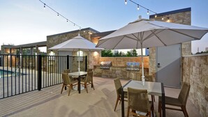 Un espace extérieur aménagé avec un barbecue, une table à manger, des chaises et des guirlandes lumineuses.