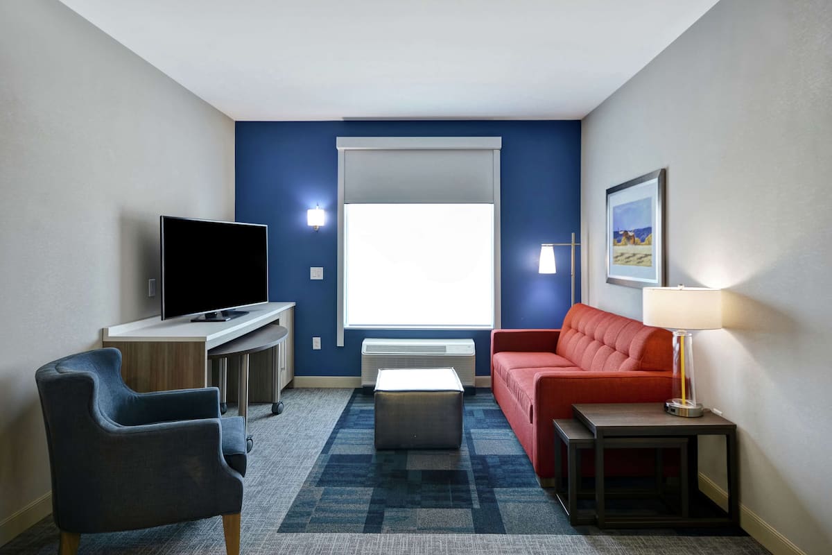 A hotel room with a flat-screen TV, a red sofa, a small table, and a lamp.