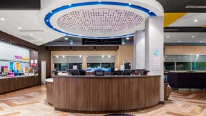 Un área de recepción moderna de hotel con un diseño circular, un mostrador de madera y un panel informativo digital.