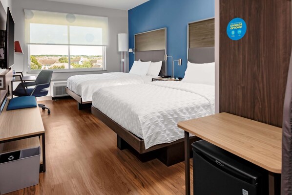 A hotel room with two beds, a desk, a chair, a small table, and a view of the outside. - Tru by Hilton Cypress Houston (Cypress)
