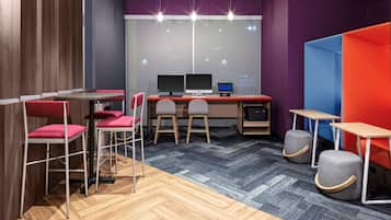 A modern office space with wooden flooring, red and grey chairs, a desk with two monitors, and a small stool.