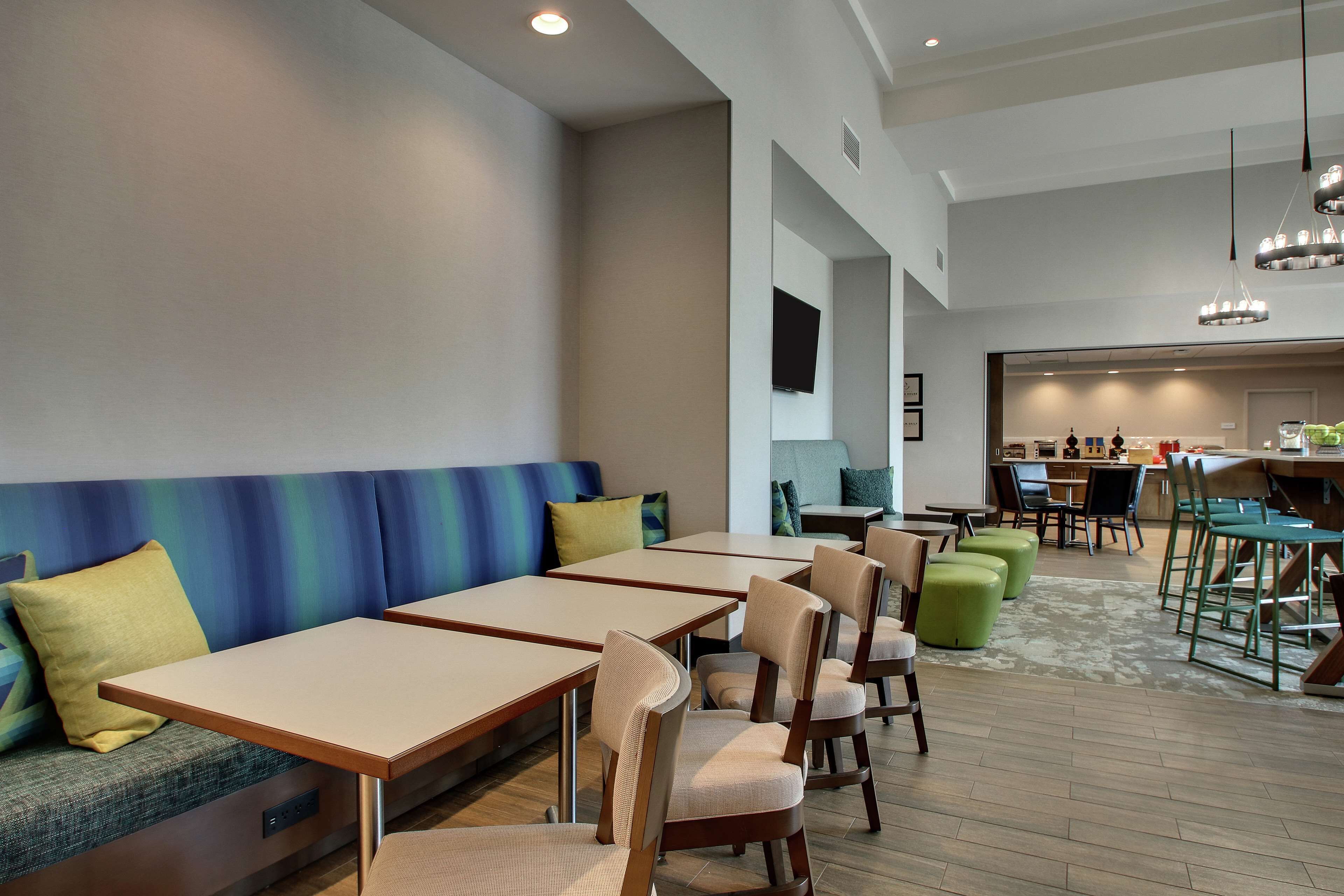 A modern dining area with booths and tables, a kitchen in the background, and a neutral color scheme.