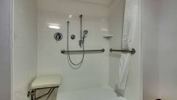 A walk-in shower with a toilet, grab bars, and a showerhead.
