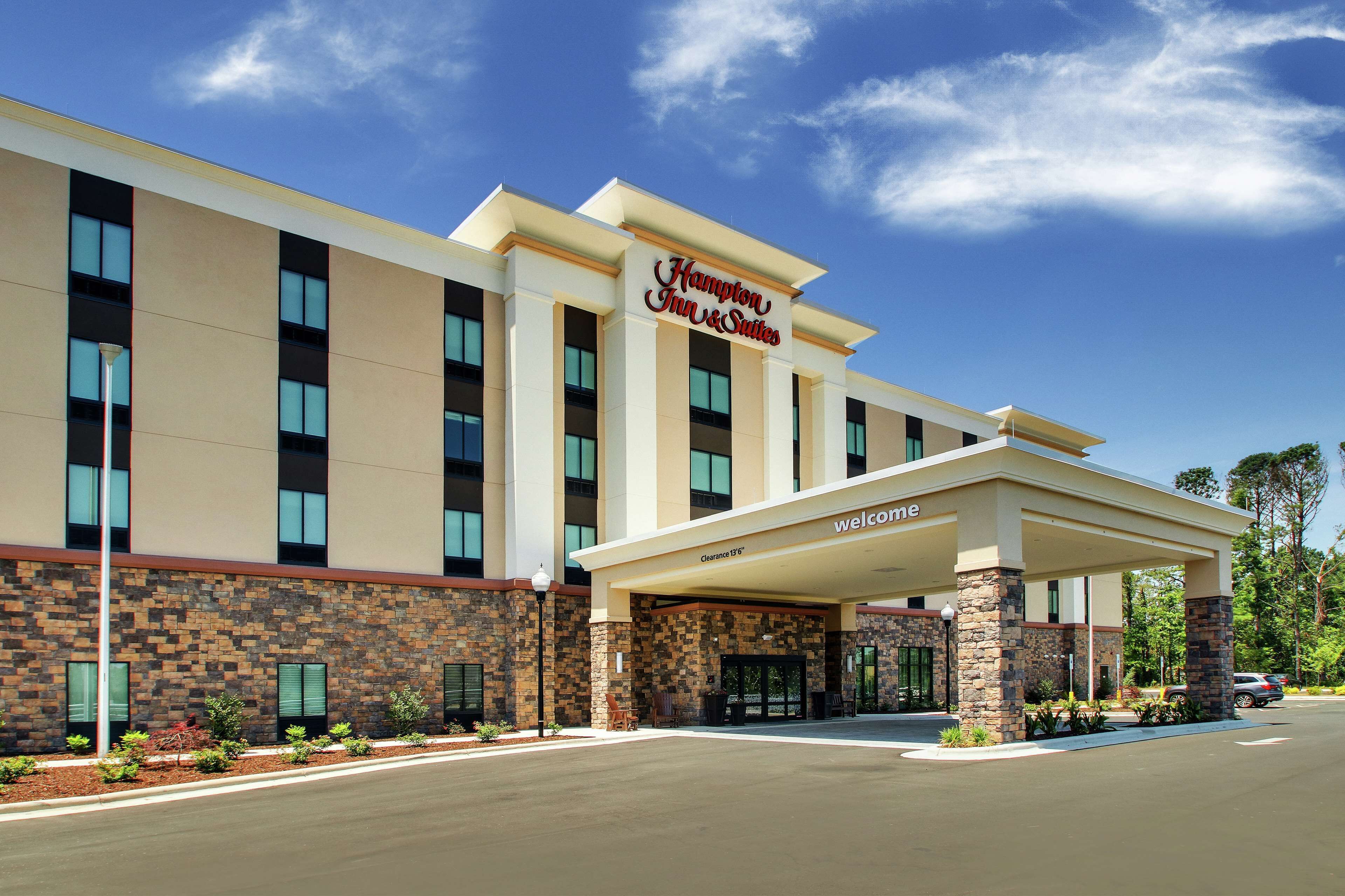 A Hampton Inn & Suites hotel with a stone facade, a covered entrance, and a clear blue sky.