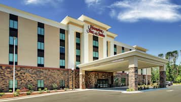 A Hampton Inn & Suites hotel with a stone facade, a covered entrance, and a clear blue sky.