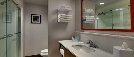 A modern bathroom with a glass shower enclosure, a white sink with a mirror, and neatly folded towels on a shelf.