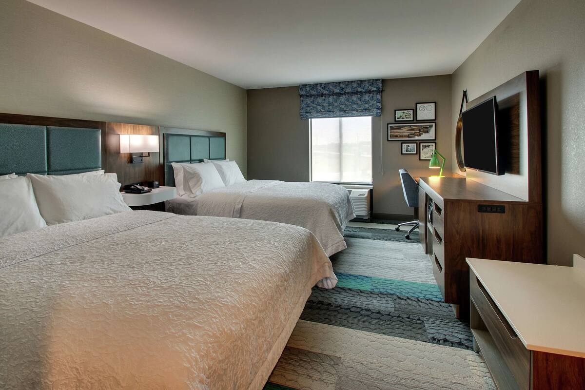 A hotel room with two beds, a desk, a TV, and a window with a view.