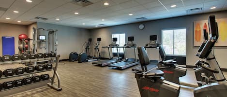 Ein Fitnessstudio mit Laufbändern, Crosstrainern und einer Hantelbank.