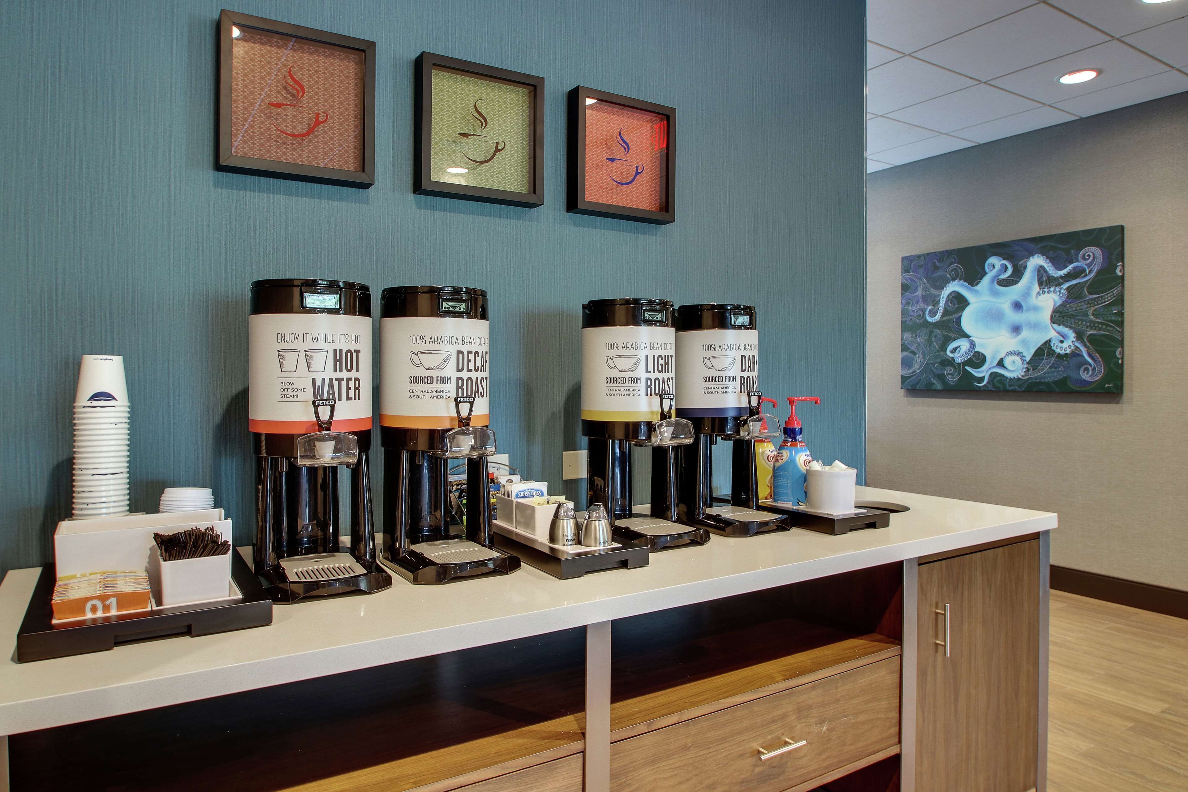 Een koffiehoek met vier koffieautomaten, een koffiemachine en een dienblad met bekers en suikerzakjes.