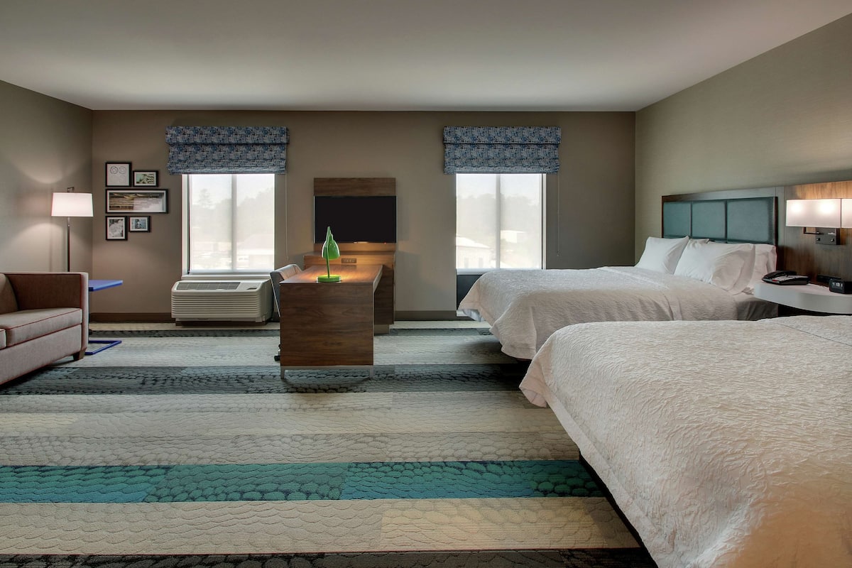 A hotel room with two beds, a desk, a chair, a sofa, a TV, and a fireplace.