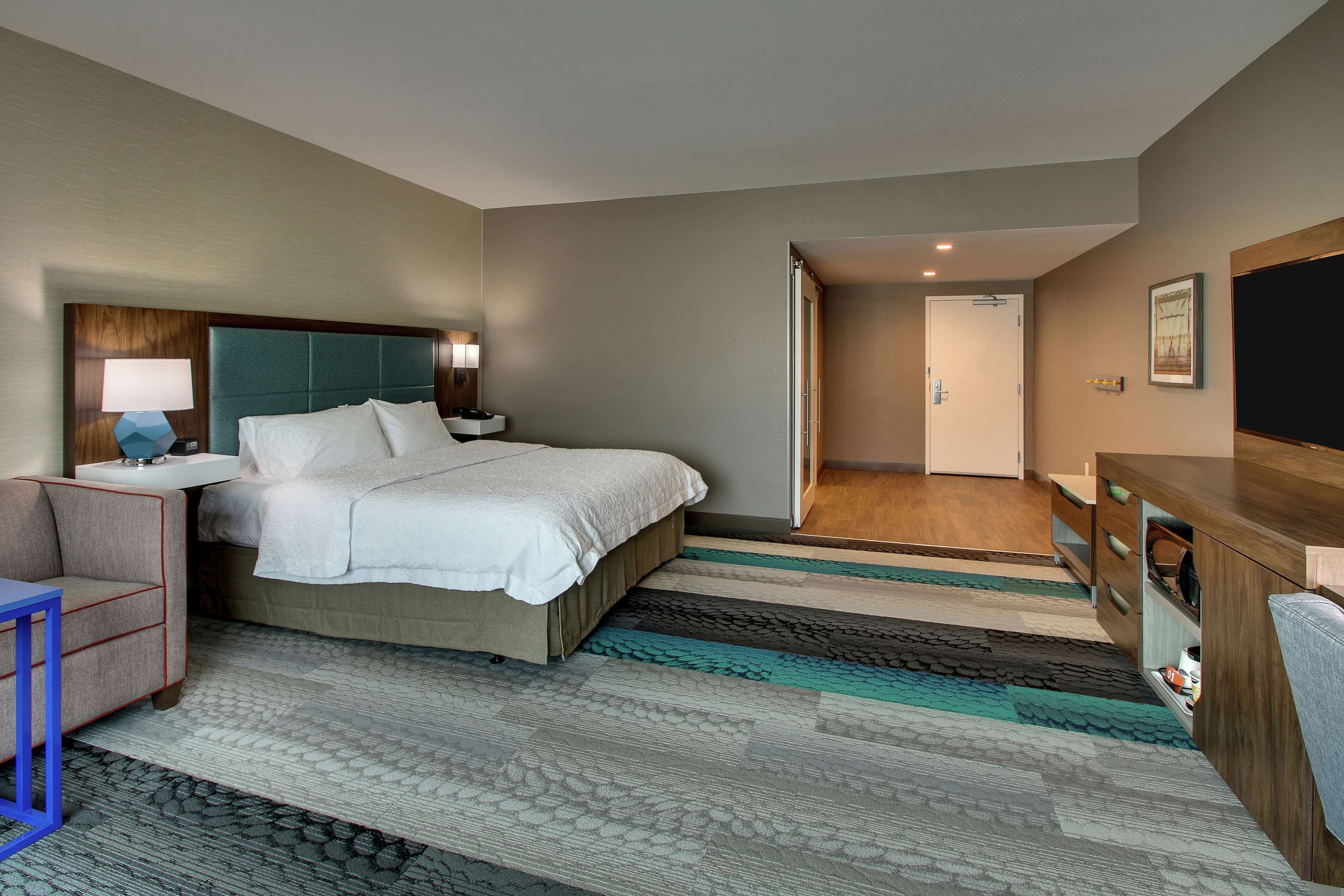 Een hotelkamer met een bed, nachtkastjes, een bureau, een stoel, een televisie en een deur die naar een andere kamer leidt.